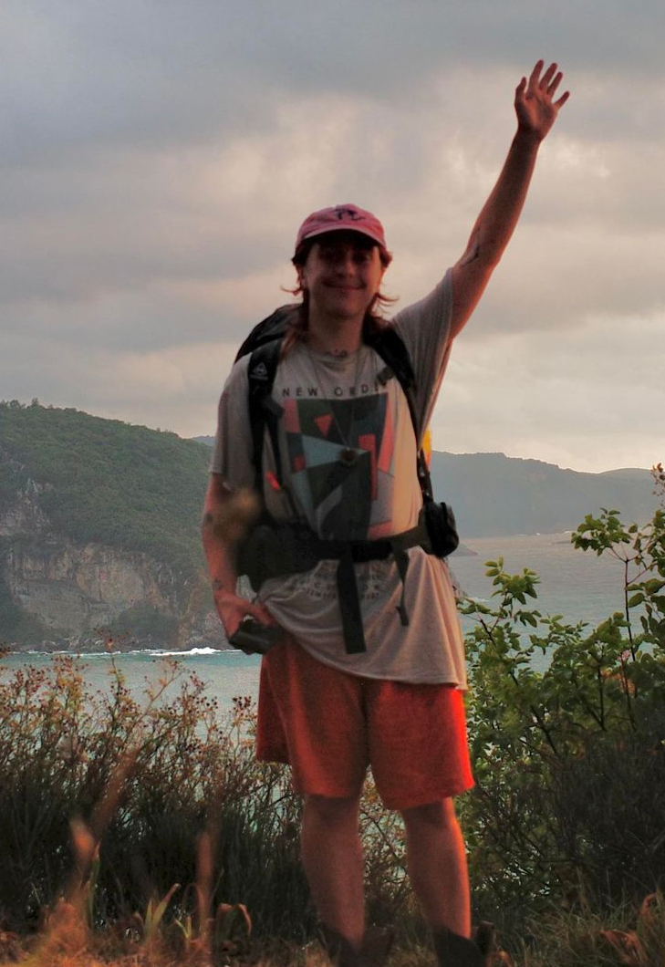 Slate, wearing a hat and backpacking backpack, waves to camera from atop a mountain overlooking the Black Sea in Turkey.